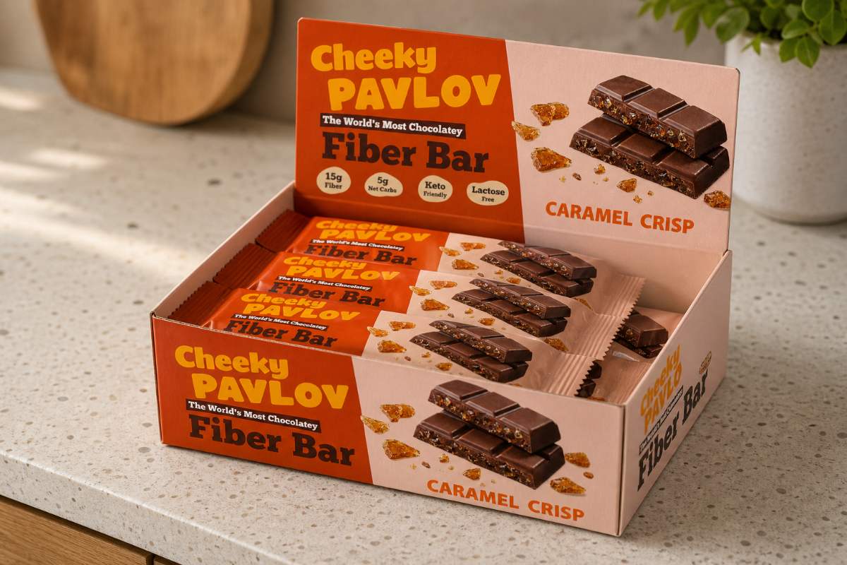 A countertop display box of Cheeky Pavlov Fiber Bars, Caramel Crisp flavor, with several individually wrapped bars visible inside. The packaging is orange and cream with product imagery of chocolate-style fiber bars with caramel crisp pieces
